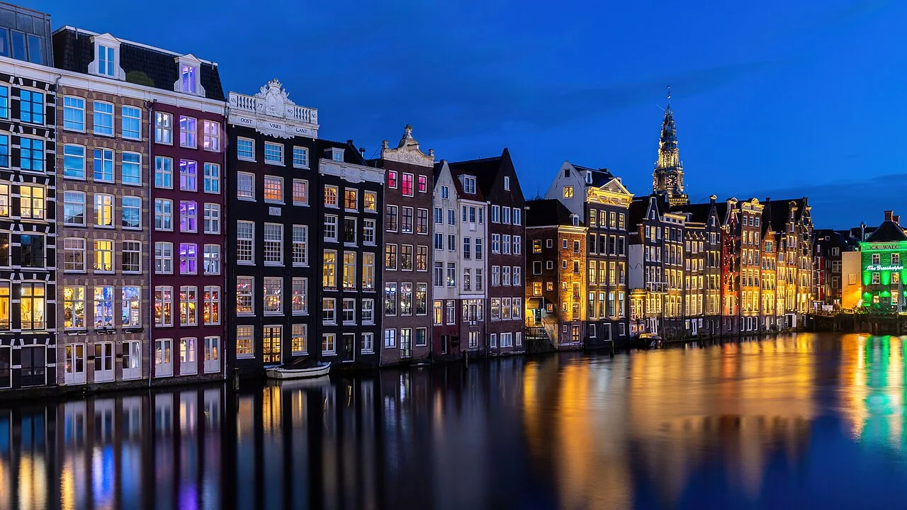 Colorful Damrak canal houses and water reflections at blue hour, photographed in April 2024; archival Amsterdam city atmosphere